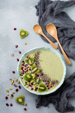 Kivi muz smoothies bir kase yulaf ezmesi, Antep fıstığı, nar taneleri ve chia ışık gri taş zemin üzerine. Seçici odak. Üstten Görünüm. Kopya alanı.