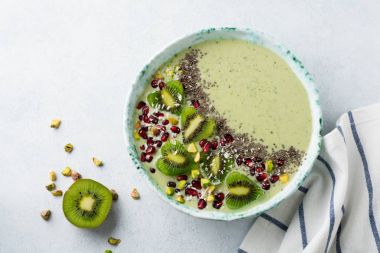 Kivi muz smoothies bir kase yulaf ezmesi, Antep fıstığı, nar taneleri ve chia ışık gri taş zemin üzerine. Seçici odak. Üstten Görünüm. Kopya alanı.