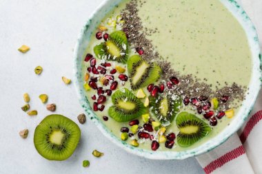 Kivi muz smoothies bir kase yulaf ezmesi, Antep fıstığı, nar taneleri ve chia ışık gri taş zemin üzerine. Seçici odak. Üstten Görünüm. Kopya alanı.