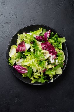 Siyah taş zemin üzerine taze yaprakları seramik plaka farklı salata. Seçici odak. Üstten Görünüm. Kopya alanı.