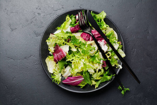 Fresh leaves of different salads in ceramic plate on black stone background. Selective focus. Top view. Copy space.