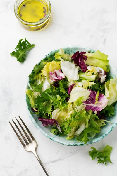 stock image Fresh leaves of different salad in ceramic plate on white stone background. Selective focus. Top view. Copy space.