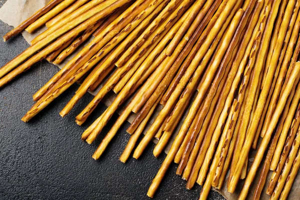 Salted bread sticks or long crunchy salty pretzel sticks on parchment paper on old brown stone or concrete background. Selective focus. Top view.