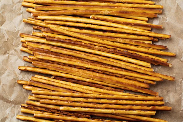Salted bread sticks or long crunchy salty pretzel sticks on parchment paper on old gray stone or concrete background. Selective focus. Top view.