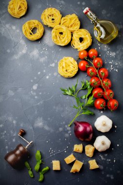 Malzemeler geleneksel İtalyan pasta yemek için. Pişmemiş ham tagliatelle bolognesi, parmesan peyniri, zeytinyağı, sarımsak, fesleğen yaprağı, biber, domates eski karanlık taş zemin üzerine. Seçici odak. Üstten Görünüm.