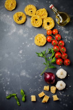 Malzemeler geleneksel İtalyan pasta yemek için. Pişmemiş ham tagliatelle bolognesi, parmesan peyniri, zeytinyağı, sarımsak, fesleğen yaprağı, biber, domates eski karanlık taş zemin üzerine. Seçici odak. Üstten Görünüm.