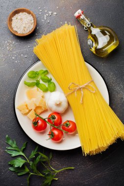 Malzemeler geleneksel İtalyan pasta yemek için. Pişmemiş çiğ makarna, parmesan peyniri, zeytinyağı, sarımsak, fesleğen yaprağı, biber, domates eski karanlık taş zemin üzerine. Seçici odak. Üstten Görünüm.