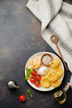 Malzemeler geleneksel İtalyan pasta yemek için. Pişmemiş ham tagliatelle bolognesi, parmesan peyniri, zeytinyağı, sarımsak, fesleğen yaprağı, biber, domates eski karanlık taş zemin üzerine. Seçici odak. Üstten Görünüm.