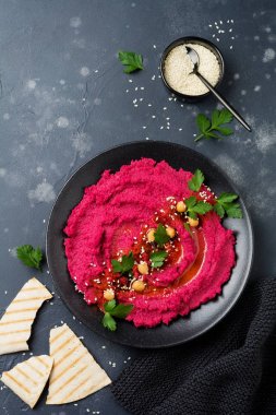 Eski karanlık beton zemin üzerine siyah seramik tabak içinde ev yapımı kırmızı pancar humus. Seçici odak. Üstten Görünüm.