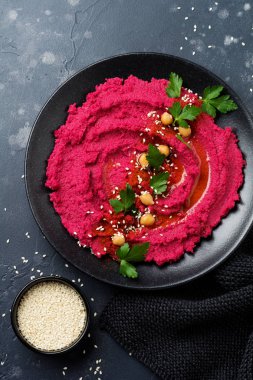 Eski karanlık beton zemin üzerine siyah seramik tabak içinde ev yapımı kırmızı pancar humus. Seçici odak. Üstten Görünüm.