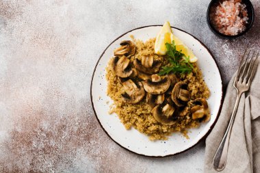 Basit seramik tabakta servis edilen sağlıklı yemek için kinoa, kızarmış mantar ve limon. Üst görünüm.