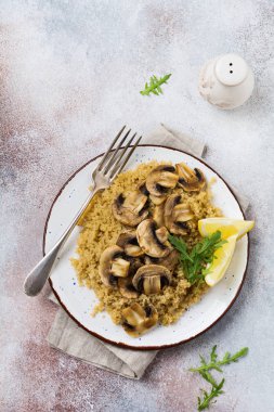 Basit seramik tabakta servis edilen sağlıklı yemek için kinoa, kızarmış mantar ve limon. Üst görünüm.