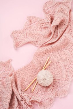 Tahta örgü iğneleri, makas ve parlak iplik. Örgü için aksesuarlar. Pembe-bej arka planda yatıyor. Üst görünüm.