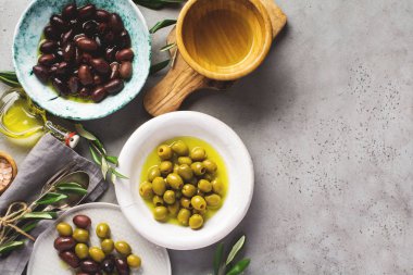 Eski, gri bir masa beton arka planında farklı seramik tabaklarda çeşitli taze zeytin çeşitleri. Doğal ürün konsepti. Kırsal kesim çatal bıçak takımı. Üst görünüm, alanı kopyala.