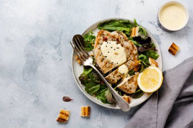 Hafif beton arka plan üzerinde bir seramik tabakta sos, brokoli, arugula ve pazı ile ev yapımı ızgara hindi biftek. Üstte görüntü.