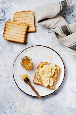 Fıstık ezmesi, muz dilimleri, bal ve badem gevreği ile tost eski bir gri beton arka plan üzerinde. Üstte görüntü.
