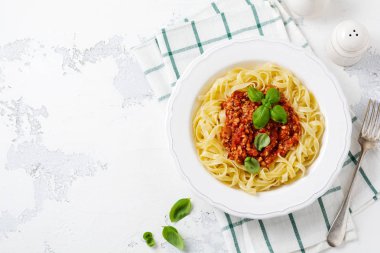 Hafif ahşap arka plan üzerinde beyaz bir tabakta bolonya sos, fesleğen ve parmesan peyniri ile geleneksel İtalyan çanak fettuccine makarna. Üstte görüntü.