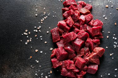 Deniz tuzu, kurutulmuş otlar ve koyu kayrak ya da beton arka planda kırmızı biberlerle sığır etini küçük parçalara ayır. Üst görünüm.
