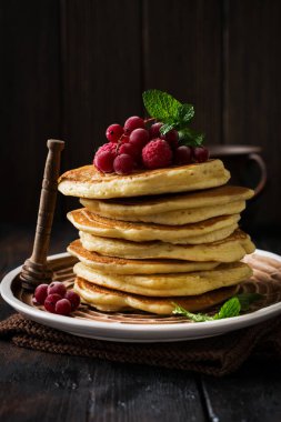Eski bir ahşap arka plan üzerinde bal, taze ahududu ve kırmızı kuş üzümü ile ev yapımı küçük krep yığını. Seçici odaklama.