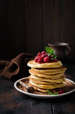 Eski bir ahşap arka plan üzerinde bal, taze ahududu ve kırmızı kuş üzümü ile ev yapımı küçük krep yığını. Seçici odaklama.