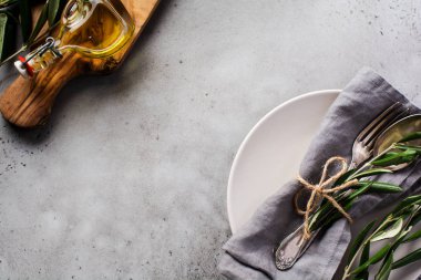 Kırsal kesim çatal bıçak takımı. Gri keten peçete, çatal ve kaşık, kırsal beton gri arka planda zeytin dalı olan tabaklar. Sonbahar tatili masa dekorasyonu seti. Üst görünüm, alanı kopyala.