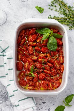 Sarımsaklı, kekik ve fesleğenli fırında kiraz domatesli beton rengi arka planda eski bir tavada. Üst görünüm.