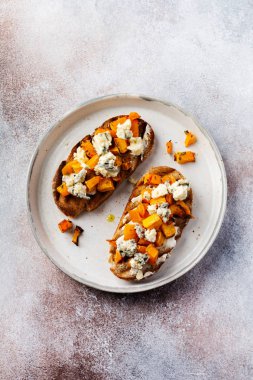 Fırınlanmış balkabağı sandviçi, mavi küflü Dorblu peynirli, bal ve kekik, beton, eski, aydınlık arka planda. Üst görünüm.