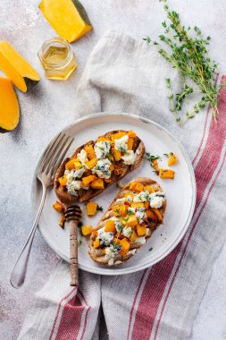 Fırınlanmış balkabağı sandviçi, mavi küflü Dorblu peynirli, bal ve kekik, beton, eski, aydınlık arka planda. Üst görünüm.