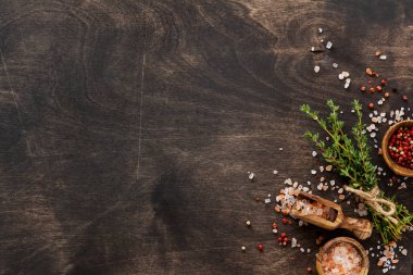 Bitkiler kekik ve baharatları eski siyah ahşap masaya yığar. Kekik, deniz tuzu ve biber. Kopyalama alanı olan üst görünüm.