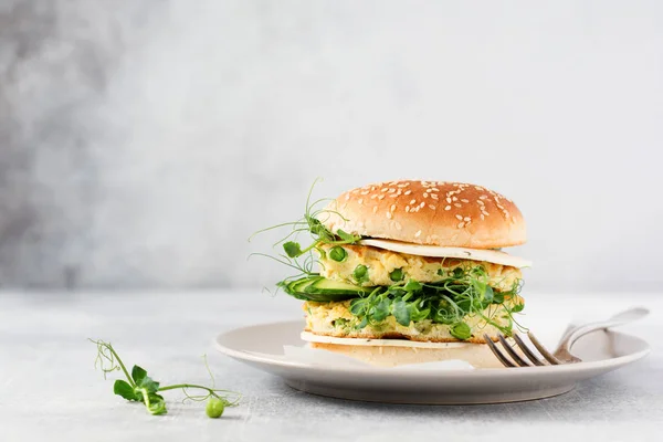 Healthy Vegetarian burger with egg and pea shoots and seeds microgreen, fresh salad, cucumber slice on a cutting wooden board on light background. Selective focus.