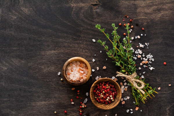 Herbs bunch thyme and condiments on old black wooden table. Thyme, sea salt and pepper. Top view with copy space.