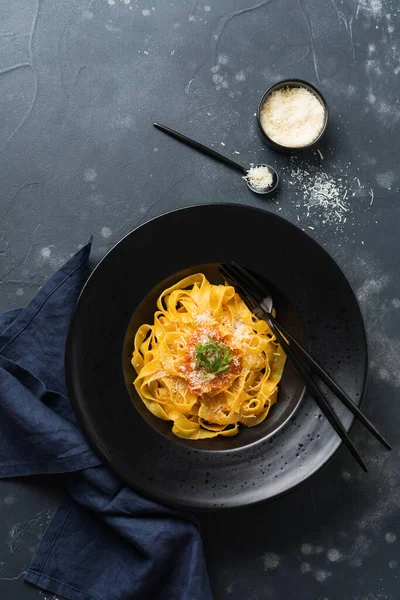 Fettuccine makarna ile geleneksel İtalyan Passat sos ve parmesan peynir koyu arka plan üzerinde siyah plaka. Üstten görünüm.