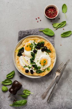 Türk yumurtaları yoğurt, peynir, zeytin, ıspanak ve gri arka planda seramik vintage tabakta kırmızı biber. Üst görünüm.