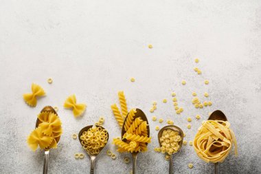 Demir kaşıklarda çeşitli makarnalar ve gri beton arka plan. Anellini makarnası. Yemek pişirme konsepti. Üst görünüm.