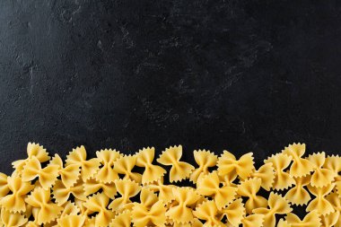 Siyah beton arka planda Farfalle çiğ makarna. Yemek pişirme konsepti. Kopyalama alanı olan üst görünüm.