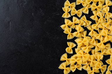 Siyah beton arka planda Farfalle çiğ makarna. Yemek pişirme konsepti. Kopyalama alanı olan üst görünüm.