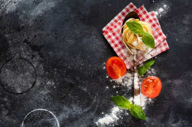 Tahta kaşıkta taze makarna, domates, çiğ yumurta ve arka plan masasında fesleğen yaprağı. Yemek pişirme konsepti. Kopyalama alanı olan üst görünüm.