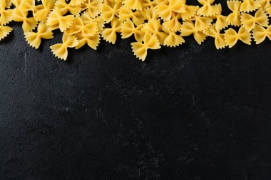 Siyah beton arka planda Farfalle çiğ makarna. Yemek pişirme konsepti. Kopyalama alanı olan üst görünüm.