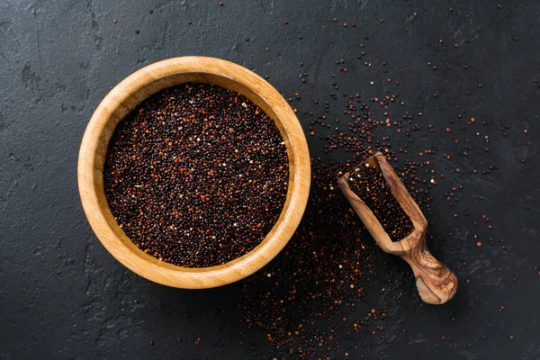 Black quinoa grains seeds in a bamboo bowl on a black stone background. Flat lay with copy space.