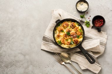 Peynirli ve krem soslu köfteler gri renkli arka planda dökme demir tavada. Üst görünüm.