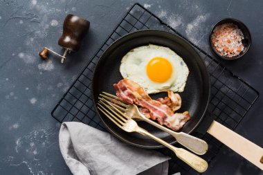 Geleneksel İngiliz kahvaltısı kızarmış yumurta ve pastırma ile koyu beton arka planda dökme demir tavada. Üst görünüm.