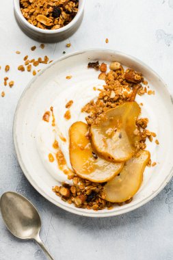 Gri seramik tabakta sağlıklı bir kahvaltı için karamelize armut, granola, fındık ve eritilmiş şeker içeren Yunan yoğurdu. Kırsal tarzda. Üst görünüm.