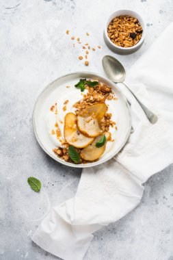 Gri seramik tabakta sağlıklı bir kahvaltı için karamelize armut, granola, fındık ve eritilmiş şeker içeren Yunan yoğurdu. Kırsal tarzda. Üst görünüm.