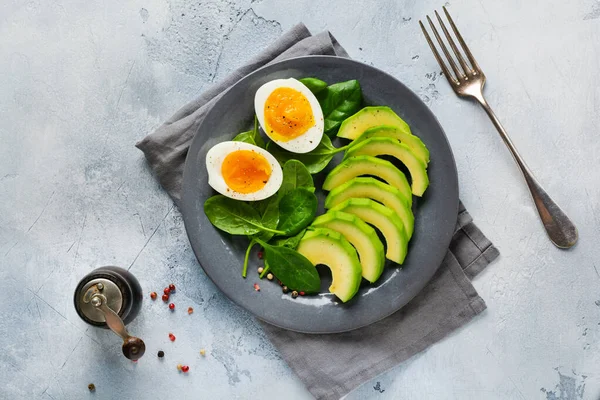 Sağlıklı vejetaryen salata kahvaltısı. Ispanak yaprakları, domates, avokado ve gri tabakta haşlanmış yumurta ve gri beton arka plan. Buda kasesi. Üst görünüm.
