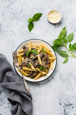 Mantarlı makarna, parmesan peyniri ve fesleğen yaprakları seramik kapta, açık beton arka planda. Seçici odak.