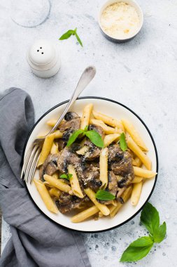 Mantarlı makarna, parmesan peyniri ve fesleğen yaprakları seramik kapta, açık beton arka planda. Seçici odak.