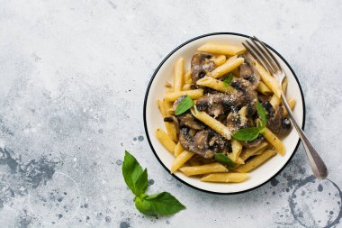 Mantarlı makarna, parmesan peyniri ve fesleğen yaprakları seramik kapta, açık beton arka planda. Seçici odak.