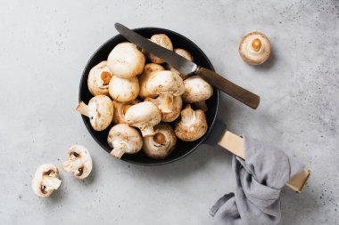 Çiğ Champignon mantarları eski beton gri bir arka planda, dökme demir bir tavada kızartılmak üzere. Üst görünüm.