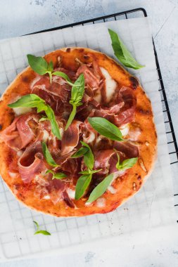 Jamonlu ev yapımı pizza, mozzarella ve arka planda taze fesleğen yaprakları. Üst görünüm.
