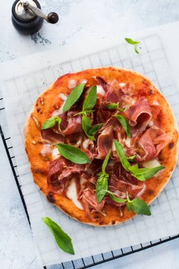 Jamonlu ev yapımı pizza, mozzarella ve arka planda taze fesleğen yaprakları. Üst görünüm.